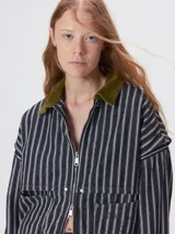 Campera de denim a rayas verticales con cuello de pana en color bordó. Presenta cierre frontal, mangas desmontables con cierre en los hombros, canesú en el pecho y bolsillos de parche cuadrados.