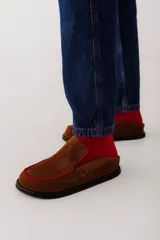 Zueco de cuero color marrón oscuro, con costuras decorativas en hilo rojo en el empeine y suela plana de goma.