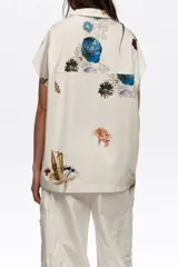 Camisa de manga corta color blanco con cuello solapa y estampado de temática marina con peces y estrellas de mar, con cierre frontal de botones y un bolsillo en el pecho.