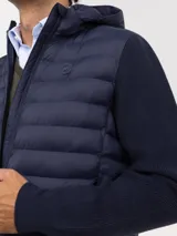 Chaqueta híbrida para hombre con frente acolchado de nylon y mangas de tejido de punto. Cuenta con cierre frontal, capucha y puños acanalados.