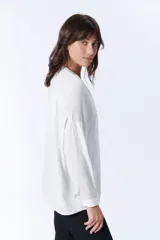 Blusa blanca de manga larga con escote en V y cierre frontal con botones.