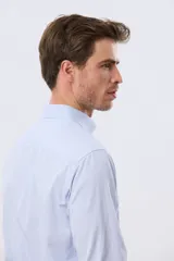 Camisa de vestir de manga larga con diseño de rayas finas celestes y blancas, cuello clásico y cierre frontal con botones. Incluye pequeño logo bordado en el pecho.
