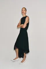 Vestido midi de Zara Woman Collection color negro, sin mangas, con cuello redondo y espalda abierta. Presenta un diseño asimétrico en el bajo adornado con flecos a tono, y cierre trasero con cremallera y botón.