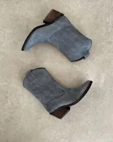 Bota corta de gamuza color marrón topo, estilo western, con bordados decorativos en hilo blanco en caña y empeine. Posee taco cuadrado de madera y punta ligeramente afilada.