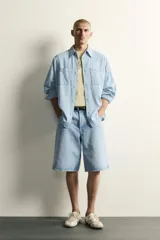 Camisa de corte relajado confeccionada en denim ligero de algodón, con cuello solapa, manga larga con puños abotonados y bolsillos de plastrón en el pecho. Presenta un acabado con efecto lavado y cierre frontal mediante botones.