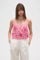 Top lencero de algodón color rosa claro, con tirantes finos y escote profundo. Presenta bordados florales grandes en color fucsia con detalles de mostacillas en el centro de las flores. El calce es holgado.