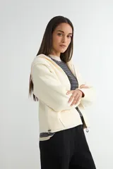 Abrigo negro con capucha, confeccionado en tejido de textura suave. Presenta cierre frontal con cremallera, bolsillos laterales integrados con costuras decorativas y puños ajustados.