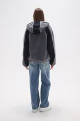 Campera de abrigo de tejido polar (tipo sherpa) color gris oscuro, con capucha y cierre frontal. Presenta paneles de color negro en los hombros y mangas, ribeteados con un vivo de color claro.