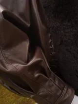 Campera oversize de cuero tostado con solapas y forro interno de corderito sintético azul marino, mangas anchas y detalles de costuras trenzadas.