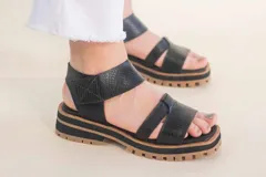 Sandalias de cuero negras con tiras cruzadas y ajuste al tobillo. Suela track color caramelo.