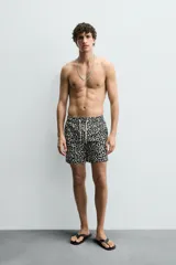 Short de baño largo con estampado geométrico en tonos oscuros sobre fondo claro, cintura elástica ajustable con cordón y bolsillos laterales.
