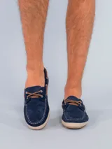 Mocasines estilo náutico de gamuza azul marino con cordones de cuero marrón. Presentan una suela con detalle de yute trenzado alrededor del borde y base de goma.