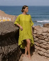 Vestido corto de lino color verde lima, de corte asimétrico más largo en la espalda, con mangas cortas amplias, escote redondo y detalle de volados en el ruedo.
