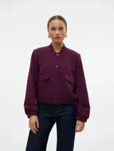 Campera bomber corta de tejido sarga color bordó, con cuello redondo estilo rib, cierre frontal de botones a presión y bolsillos frontales con solapa. Presenta mangas largas con puños elásticos y elástico en el ruedo.