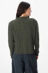 Saco corto de tejido de punto con diseño de trenzas, cuello con detalle de volado y cierre frontal con botones. Presenta mangas largas y ajuste al cuerpo.