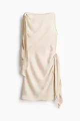 Vestido corto de satén color beige, sin mangas, con escote bote y detalles de tiras para anudar en el hombro y la cintura.