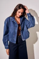 Campera bomber de jean con corte oversize, cierre frontal y cuello alto con botones a presión. Presenta mangas amplias y puños ajustados.