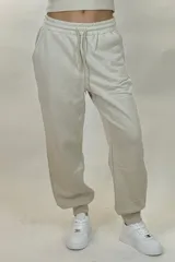 Pantalon deportivo tipo babucha de color beige, con cintura elástica ajustable mediante cordón y puños elásticos en los tobillos.
