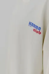 Remera color crema de corte holgado, con cuello redondo y estampado pequeño en el pecho con la frase 'Karma Club' en azul y rojo.