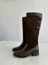 Bota alta de cuero color marrón chocolate, con taco cuadrado de 5 cm y caña alta hasta la rodilla. Presenta tres correas con hebillas en la parte superior de la caña. Fabricada en Colombia.