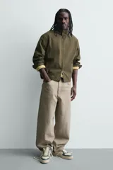 Zapatilla deportiva de estilo retro con diseño de paneles en combinación de colores crema, verde azulado y detalle en rojo en el talón. Presenta suela con volumen y cierre con cordones.