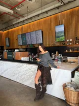 Buzo de tejido de punto color negro con diseño asimétrico y escote tipo hombros caídos. Presenta un detalle de aro metálico plateado en el frente que genera un drapeado artesanal y elegante.