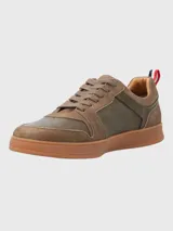Sneaker de hombre en tonos marrones, confeccionada en una combinación de cuero y descarne. Presenta un diseño de paneles con cordones al tono, suela de goma color caramelo y un detalle de cinta tricolor en el talón.