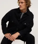 Campera de hombre de jean negro, modelo regular, con cuello inglés, abotonado frontal, dos bolsillos con solapa en el pecho y manga larga ajustada.