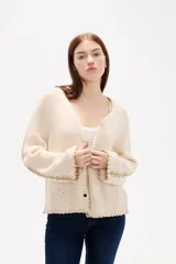 Cardigan de punto color natural, con cuello en V, cierre frontal con botones y diseño holgado. Presenta detalles de costuras decorativas bordadas a lo largo de las mangas y en los bordes.