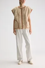 Chaleco reversible oversize de tejido tipo corderito, color beige con detalles de costuras y ribetes en marrón y cierre frontal con cremallera.