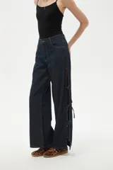 Pantalon de jean azul oscuro de corte ancho y tiro bajo, con detalle de aberturas laterales ajustables mediante lazos.