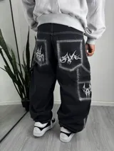 Pantalón baggy negro de estilo cargo, con efecto acid wash y costuras en contraste. Presenta grandes bolsillos traseros y en las piernas, decorados con bordados en blanco de diseño gótico y abstracto.