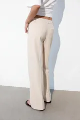 Pantalón de corte recto y tiro bajo, color marrón oscuro. Presenta trabillas en la cintura, bolsillos laterales, falsos bolsillos traseros de vivo y raya planchada en el delantero. Cierre frontal con cremallera, botón interior y ganchos metálicos.