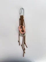 Charm para bolso o accesorios con mosquetón metálico, tejido de macramé en cordón negro y dijes de cerámica esmaltada en tonos violeta y celeste.