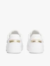 Zapatillas de tenis de corte bajo confeccionadas en piel de color blanco. Presentan un diseño clásico con cordones, una insignia metálica con el monograma TH en el lateral y un panel metalizado en el talón. Incluyen detalles distintivos de la marca Tommy Hilfiger en la lengüeta y el lateral, con suela de goma blanca.