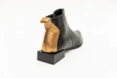 Botín corto de cuero negro con detalle de cuero dorado en el talón y textura de cocodrilo en el lateral. Tiene cierre lateral y taco cuadrado.