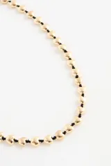 Collar largo con cuentas en forma de corazón color dorado, ensartadas en un cordón rojo.