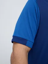 Remera polo deportiva Umbro del Club Nacional de Football, color azul con cuello en V y detalles en rojo y blanco. Incluye el logo de Umbro y el escudo del club.