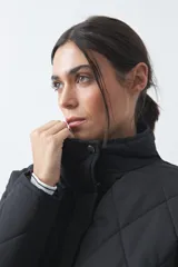 Campera capitoneada de largo medio, color negro, con cuello alto, cierre frontal con cremallera y broches a presión, y bolsillos laterales con solapa.