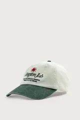 Gorra de seis paneles con efecto lavado, de color blanco crudo con visera en verde militar. Presenta un bordado frontal contrastante con texto en negro y una estrella roja.