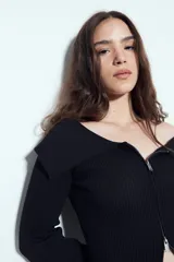 Top de punto acanalado negro, con diseño off-shoulder y escote amplio. Presenta mangas largas y cierre frontal completo con doble cursor, permitiendo ajustar la apertura superior e inferior.