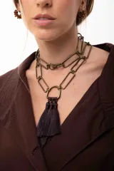 Collar de eslabones rectangulares en tono bronce, con diseño versátil que permite usarlo largo o doble. Presenta un dije central en forma de herradura con tres borlas colgantes de hilo en color marrón oscuro.