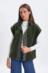 Chaleco de sherpa color verde con cuello alto y cierre frontal mediante botones a presión. Presenta una solapa central de tela técnica a tono y bolsillos laterales.