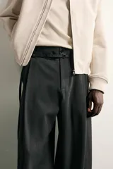 Pantalón de corte balloon fit en color gris oscuro, confeccionado en tejido con viscosa. Presenta pliegues frontales, cintura ajustable con cinturón integrado, bolsillos laterales y bolsillos traseros de doble vivo. Cierre frontal con cremallera y botón.