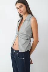 Top sin mangas con cuello camisero, escote en V profundo y detalle fruncido en los laterales. Confeccionado en tejido a rayas.