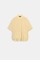 Camisa de corte fluido con cuello solapa y manga corta con dobladillo. Presenta cierre frontal con botones ocultos bajo una tapeta.