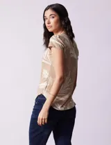 Remera color beige con estampado de hojas blancas, cuello redondo y mangas cortas.
