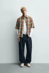 Camisa de corte boxy fit confeccionada en tejido de algodón, con estampado de cuadros en tonos tierra. Presenta cuello solapa, manga corta y cierre frontal de botones.