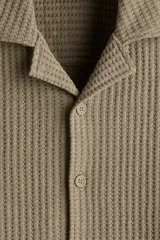 Camisa color caqui de manga corta con cuello resort y tapeta con botones. Tejido de punto waffle con corte holgado.