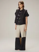 Chaleco negro con diseño de alamares frontales, costuras a la vista en contraste y volados en los hombros.